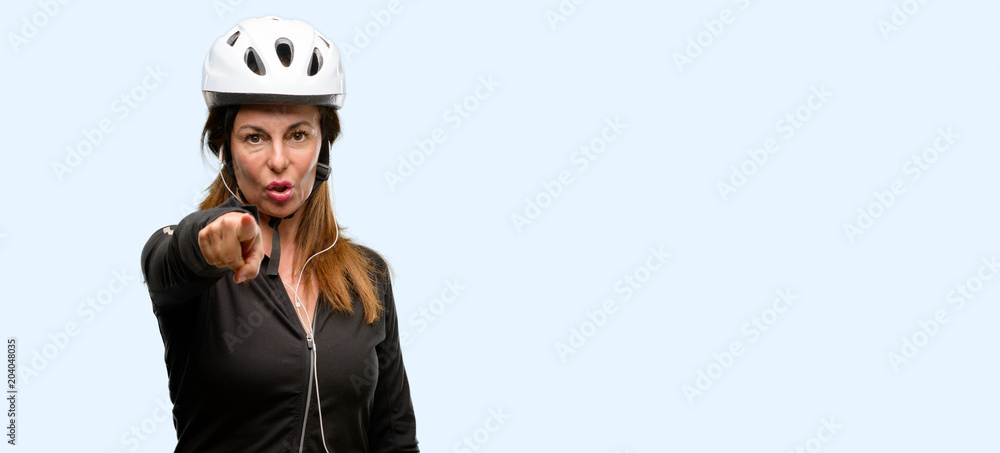 Middle age cyclist woman using earphones pointing to the front with finger isolated blue background Middle age cyclist woman using earphones pointing to the front with finger isolated blue background