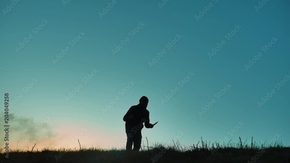 silhouette of a man in a hood with a knife. Shadow blur of horror man in jacket with hood facing side body and show the knife in his hand. A dangerous thug lifestyle with a knife killer bandit silhouette of a man in a hood with a knife. Shadow blur of horror man in jacket with hood facing side body and show the knife in his hand. A dangerous thug lifestyle with a knife killer bandit