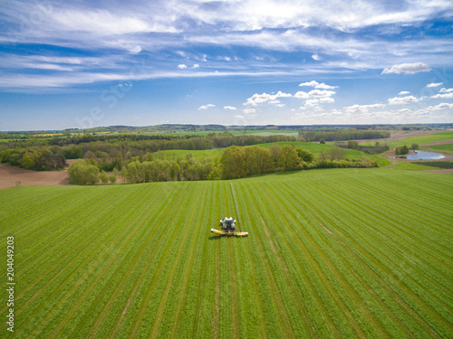  Aerial view of two modern tractors mowing a green fresh grass field on a sunny day with blue sky. 