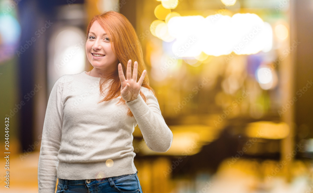 Beautiful young redhead woman raising finger, is the number four at night