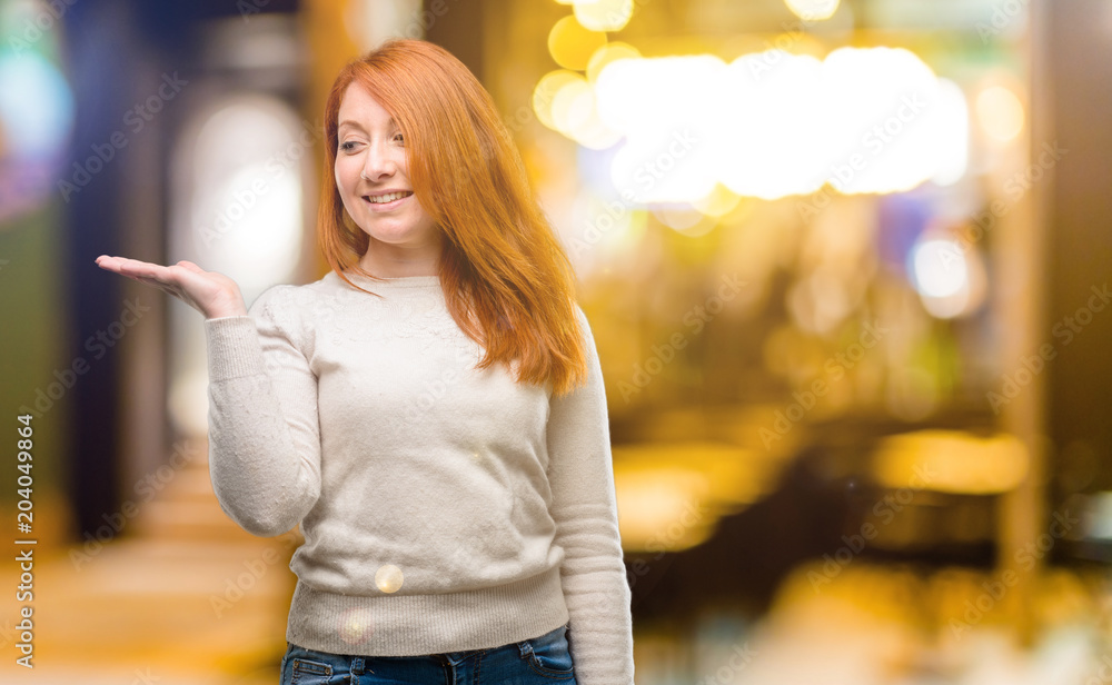 Beautiful young redhead woman holding something in empty hand at night