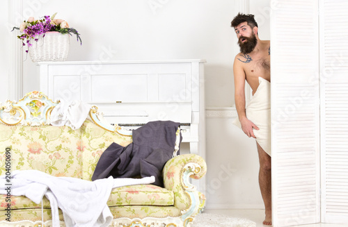 Man, lover in white interior caught naked. Man with beard and mustache hiding behind folding screen. Hipster naked on shocked face unexpectedly detected in bedroom. Lovers and cheating concept.