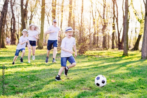 Family playing football on green grass in park. © Daniel Jędzura