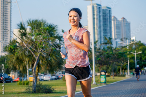 Smiling asian woman in sportswear running. Skyscreapers in a background photo