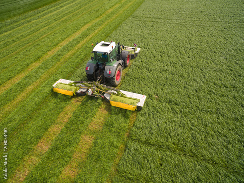Aerial view of a tractor mowing a green fresh grass field, 
a farmer in a modern tractor mowing a green fresh grass field on a sunny day