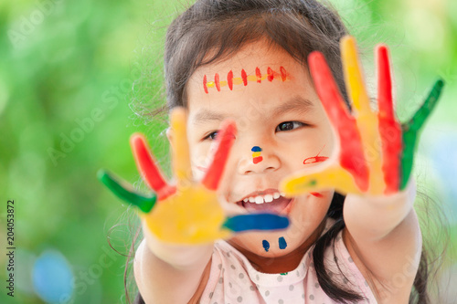 Cute asian little child girl with painted hands smiling with fun and happiness on yellow nature background