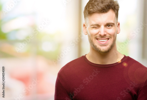 Handsome young man blinking eyes with happy gesture