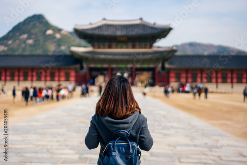 Young asian woman traveler with backpack traveling into the Gyeongbokgung Palace  with blue sky and clouds at Seoul city, South Korea.