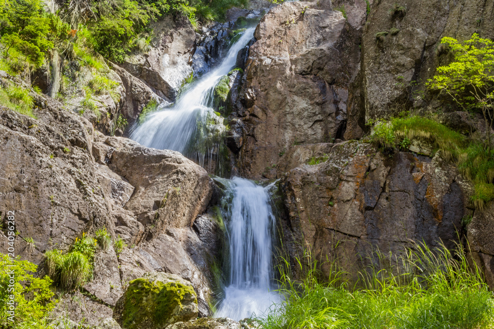Waterfall of a small stream on the cliff side, with green vegetation.