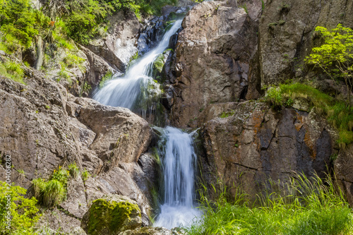 Waterfall of a small stream on the cliff side  with green vegetation.