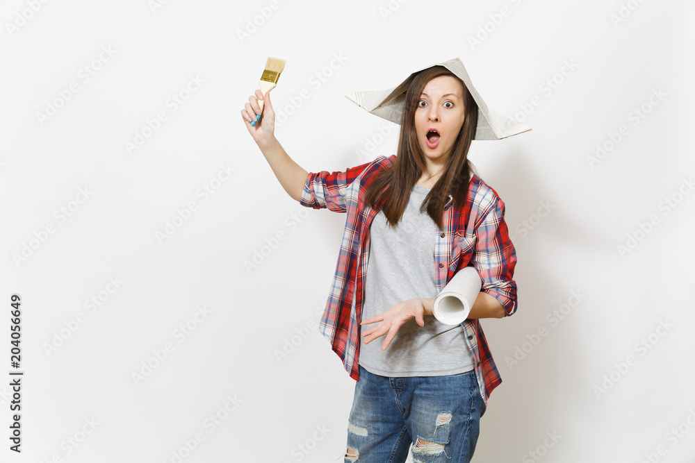 Young shocked beautiful woman in casual clothes and newspaper hat holding paint brush and wallpaper roll isolated on white background. Instruments for renovation apartment room. Repair home concept.