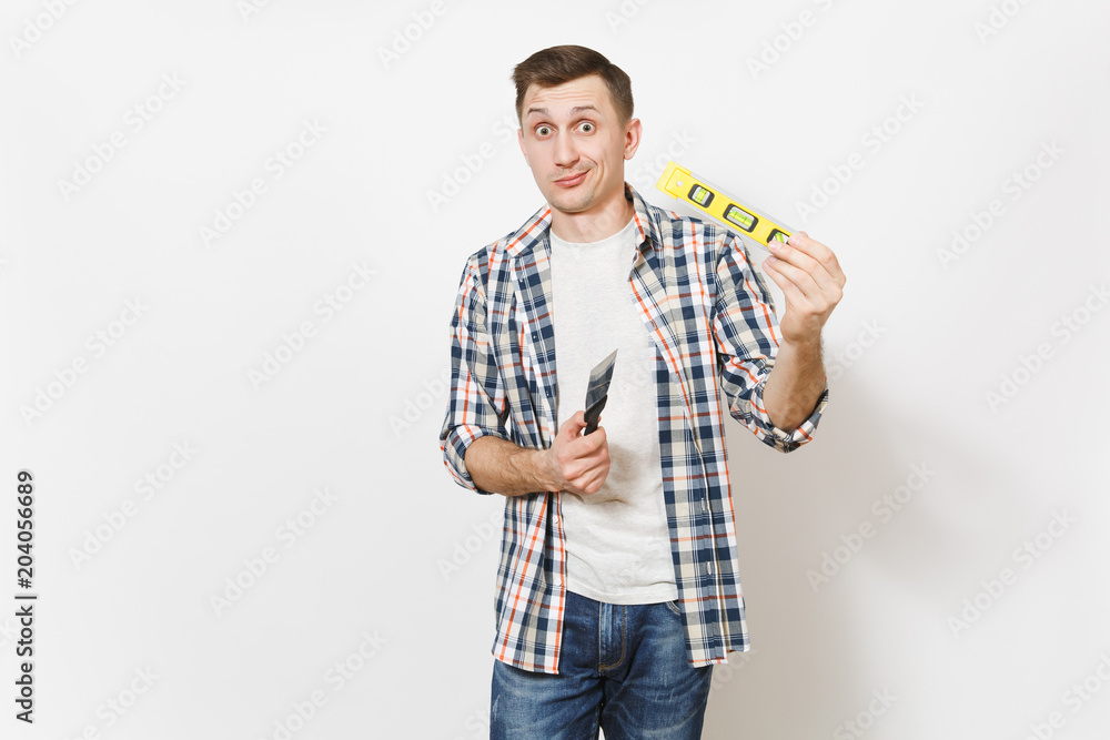 Young concerned handsome man in casual clothes holding putty knife and building bubble spirit level isolated on white background. Instruments for renovation apartment room. Repair home concept. Young concerned handsome man in casual clothes holding putty knife and building bubble spirit level isolated on white background. Instruments for renovation apartment room. Repair home concept.