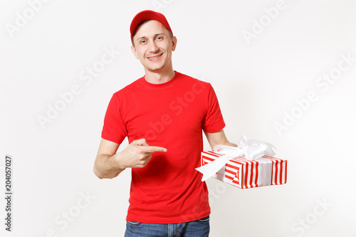 Delivery man in red uniform isolated on white background. Smiling male in cap, t-shirt, jeans working as courier or dealer, holding red striped gift box with present. Copy space for advertisement.