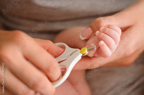 Closeup mother   s hands with nail scissors trimming her baby fingernails. Nursing a child. Mother   s care and baby   s healthy life