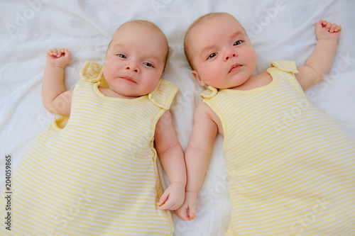 Two adorable twin babies lying down on white sheet in yellow sleeping sacks ready to go to bed. Safe sleep for babies. Infants in wearable blankets