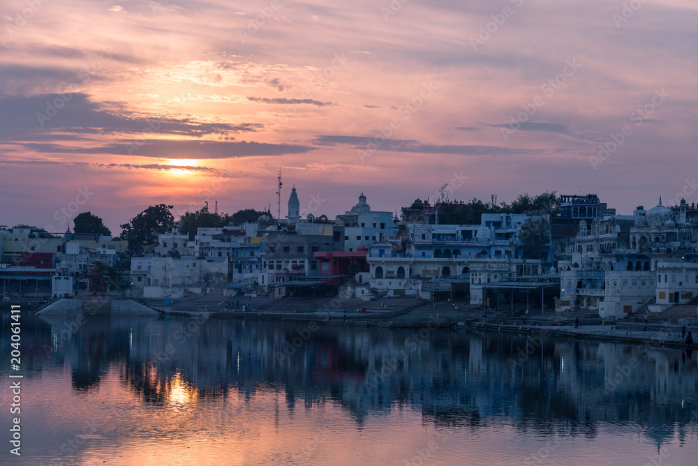 Colorful sky and clouds over Pushkar, Rajasthan, India. Temples, buildings and colors reflecting on the holy water of the lake at sunset.
