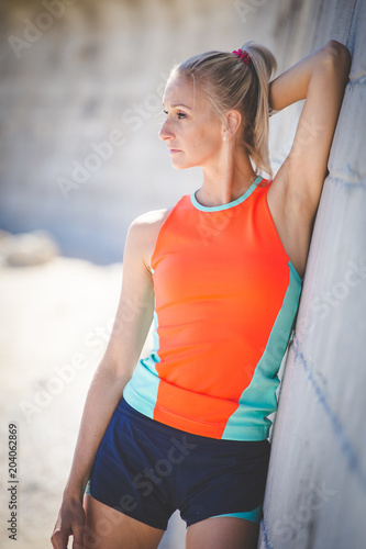 Beautiful blond fitness model resting after a workout by the beach