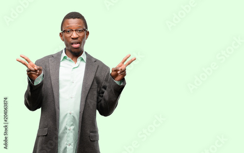 African black man wearing jacket looking at camera showing tong and making victory sign with fingers