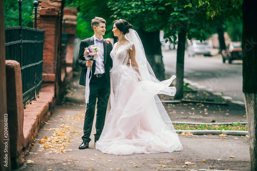 A loving couple of newlyweds walks in the city. Husband and wife on a walk. Bride and groom hug and kiss each othe at athe street. Adorable couple.