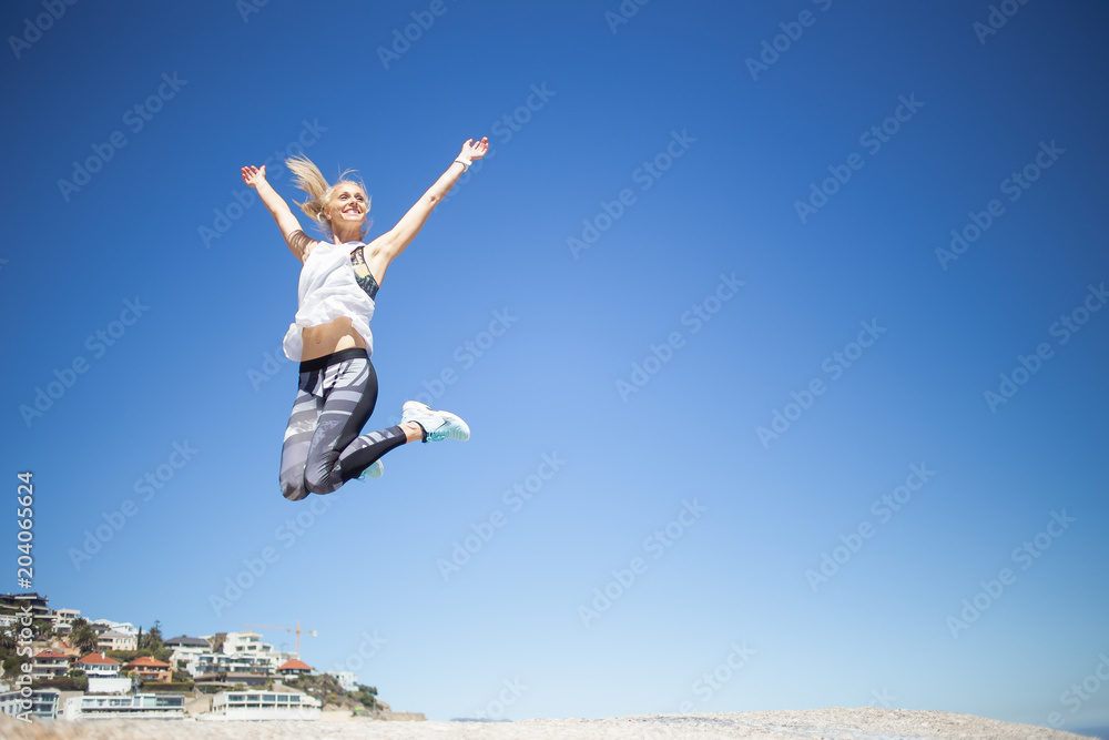 Beautiful blond female fitness model jumping from one rock to another on a bright sunny day Beautiful blond female fitness model jumping from one rock to another on a bright sunny day