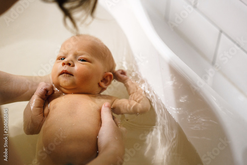 Fotografija The newborn swims in the bathroom in the arms of the mother