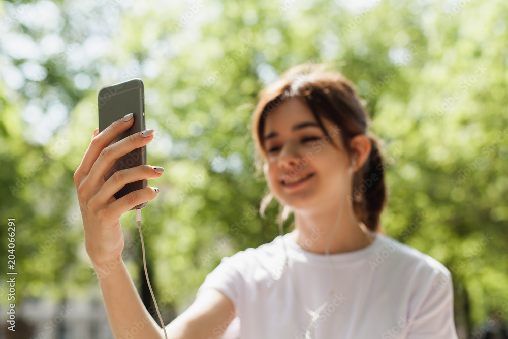 Young girl having a video talk on mobile phone sitting outdoors in the park, female hand holding phone and video talking, concept of internet and distant talking via modern gadgets