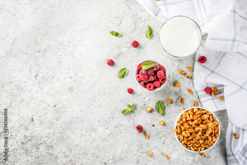 Healthy breakfast ingredients. Breakfast cereal, milk or yogurt glass, raspberries and mint on grey stone background, copy space top view