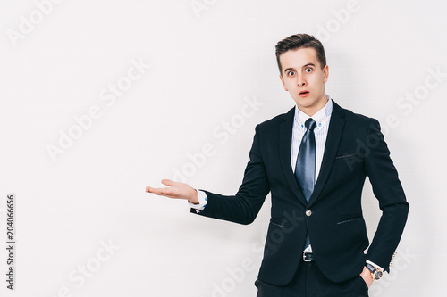Close up portrait of surprised young businessman\stock-market broker keeping palm up and pointing on it, on white background.