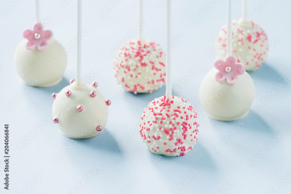 Tasty white wedding cake pops decorated with sprinkles on blue background in backlit.