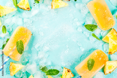 Homemade Pineapple Popsicles on Ice with fresh Pineapple slices and mint, on light blue background copy space top view frame