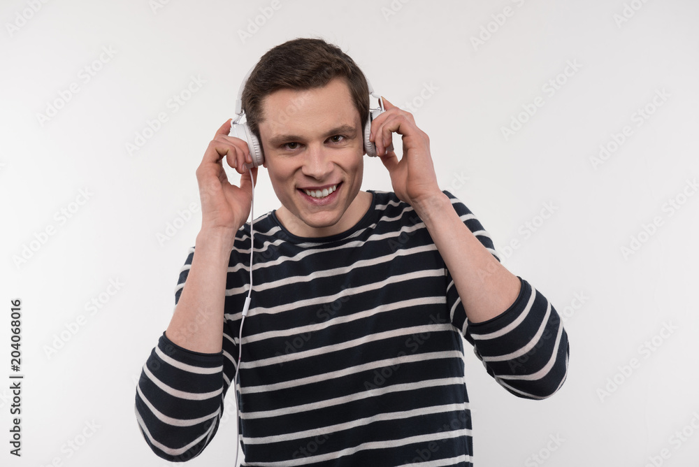 Music time. Joyful positive man smiling while putting on headphones Music time. Joyful positive man smiling while putting on headphones