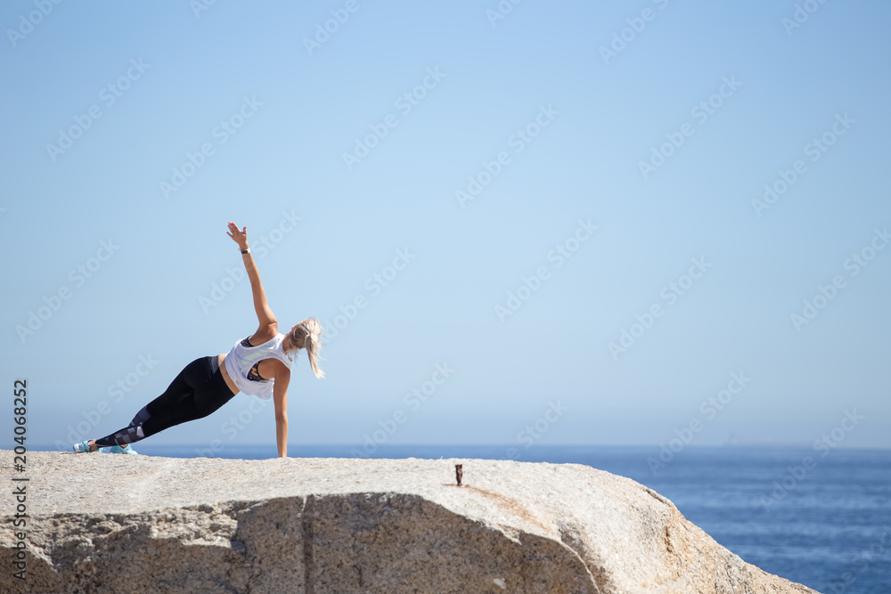 Blond female fitness model meditating and doing yoga on a granite rock overlooking the ocean