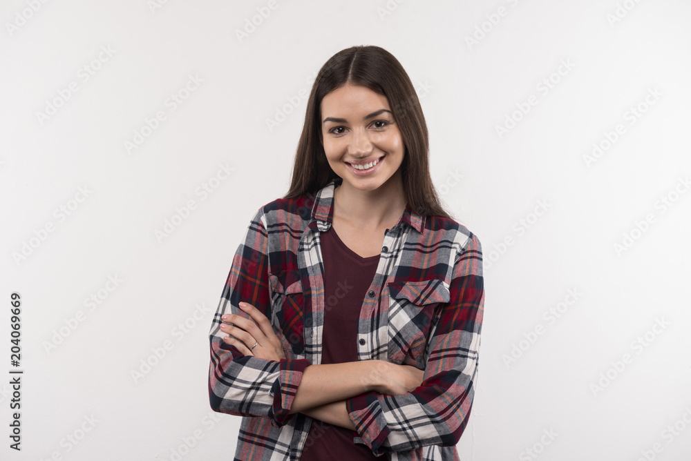 Positive emotions. Happy young woman smiling to you while standing with her arms crossed Positive emotions. Happy young woman smiling to you while standing with her arms crossed
