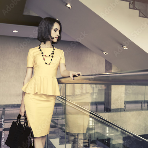 Young fashion business woman in yellow peplum dress with handbag at office photo