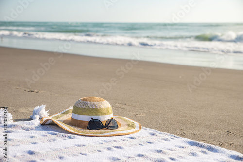 Fototapeta Naklejka Na Ścianę i Meble -  Hat on a blanket on sandy beach with ocean wave in background