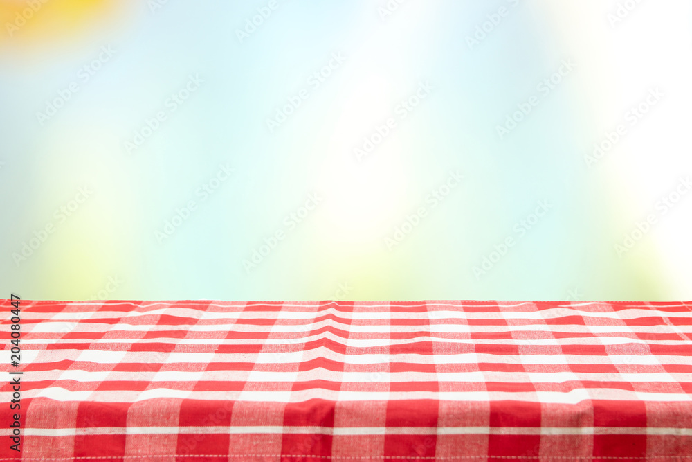 An empty table with a red checkered tablecloth and an pastel colorful natural background on a  sunny day. For your food and product display montage.