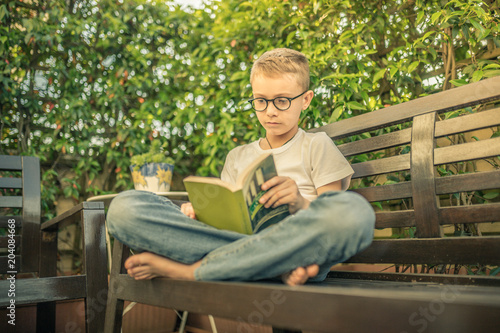 Young boy enjoy a book and relaxing in a beautiful sunny day. Pre teen alone sitting on the bench reading a bast. A beautiful spring day is ideal for relaxing in the garden doing what you like best © Fabio Principe