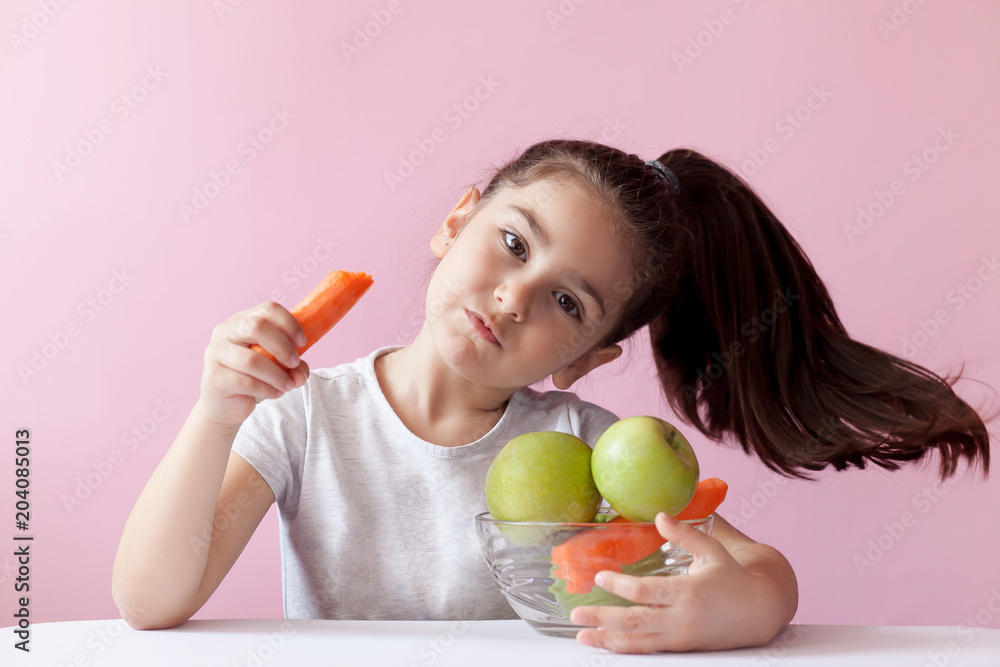 A cute little girl eating fresh vegetables. A portrait on pastel background. Healthy teeth. A cute little girl eating fresh vegetables. A portrait on pastel background. Healthy teeth.