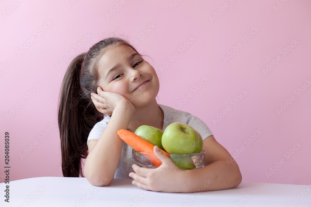 A cute little girl eating fresh vegetables. A portrait on ? pastel background. Healthy teeth. A cute little girl eating fresh vegetables. A portrait on ? pastel background. Healthy teeth.