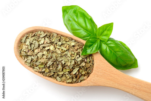 dried basil leaves in the wooden spoon, isolated on white, top view