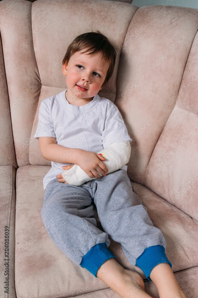 Fototapeta premium a small boy is sitting on a chair with a broken arm, in a cast. hospital. medicine. danger. pain. to break limbs. violence.