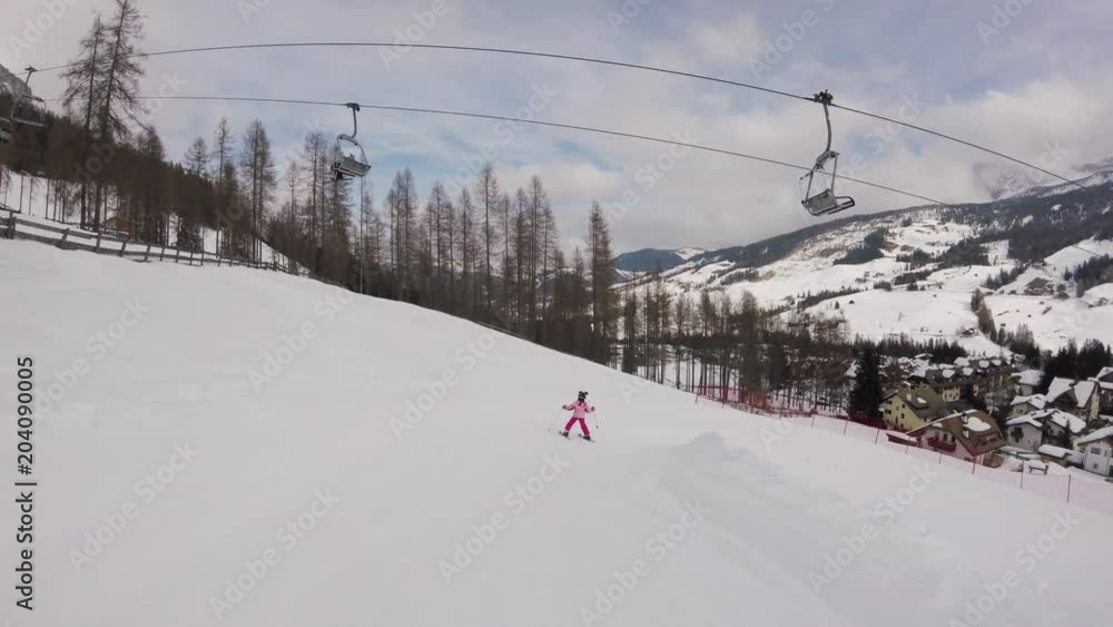 February 2018, La Villa, Italy - Little girl skiing with a beautiful view on a village in mountains February 2018, La Villa, Italy - Little girl skiing with a beautiful view on a village in mountains