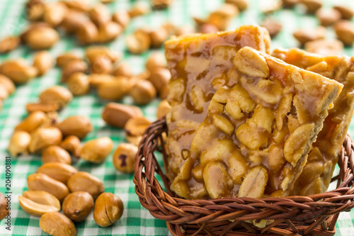 Candy with peanut: Pe de Moleque in Brazil and Chikki in India. Sweet food of Festa Junina, a typical brazilian party. Snack on wicker basket and green background. photo