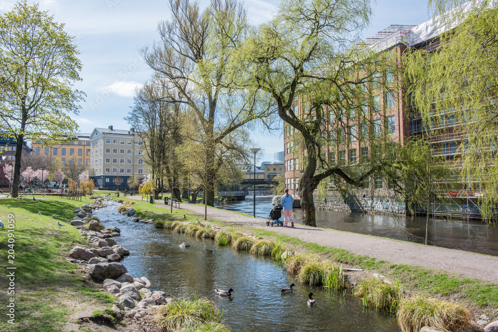Unrecognizable people enjoy waterfront park Strömparken along Motala river in Norrkoping during spring in Sweden.