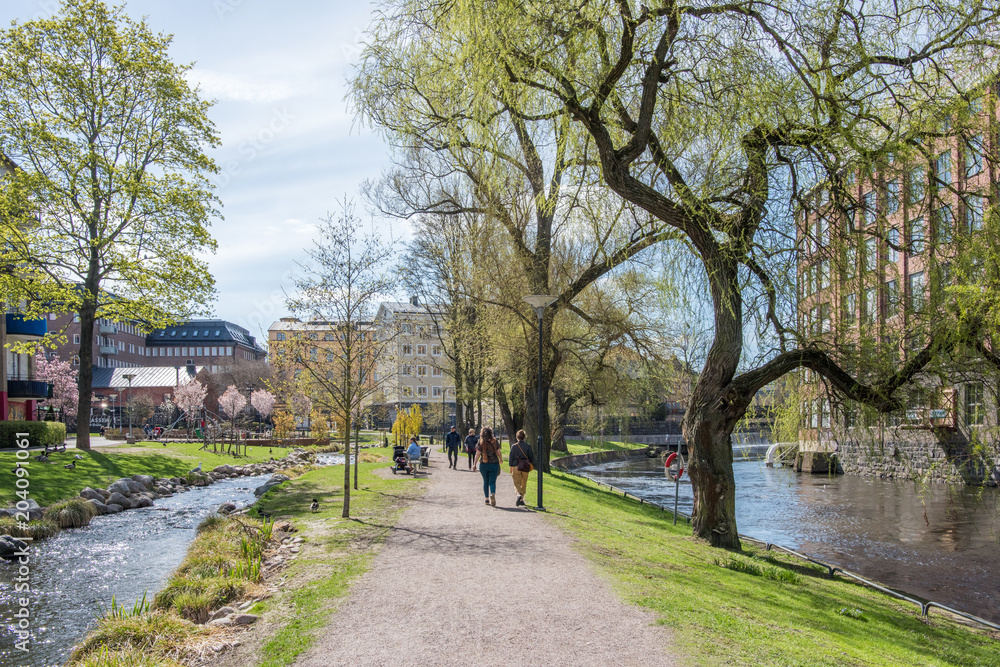 Unrecognizable people enjoy waterfront park Strömparken along Motala river in Norrkoping during spring in Sweden.