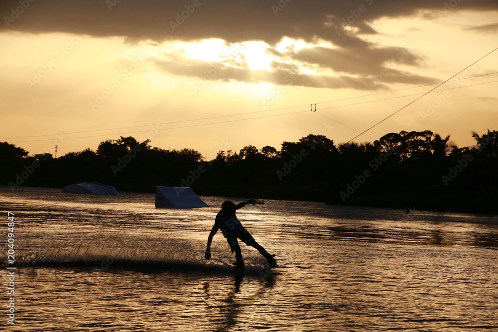 Wake Boarder Waterskiing Leaning Low Touching the Water Silhouetted Against Sunset with Ramps in the Background, Quiet Waters Park Lake, Deerfield Beach, Florida
