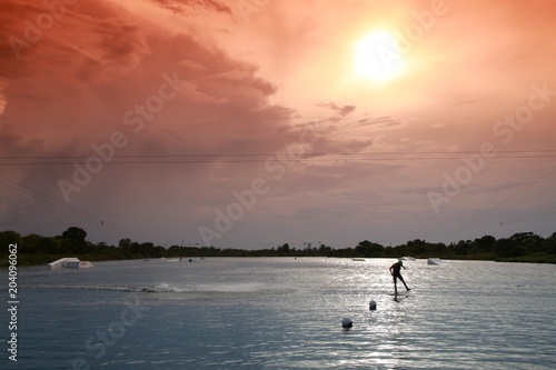 Wakeboarder Doing Half-Flip Being Pulled by Cable on Lake Against Late Afternoon Sun through Orange Graduated Filter