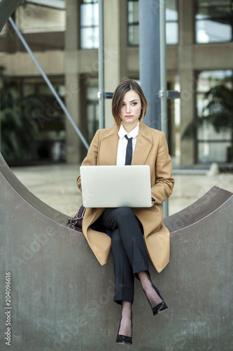 Donna d'affari con cappotto beige, lavora al computer in uesterni con aria seriosa