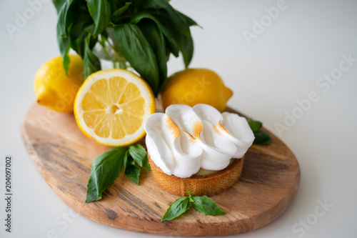 Lemon tartlets with basil on wooden desk and Cup of coffee on white table. Tasty treat on a light blue background.