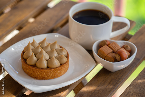 tartlet with nuts and caramel on white plate with cup of coffe